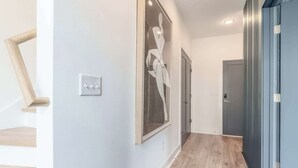 A hallway with a wooden staircase on the left, a framed artwork on the wall, and a door at the end. - Fall in Nashville: hot tub, skyline views, sleeps 12 near Broadway (Nashville)