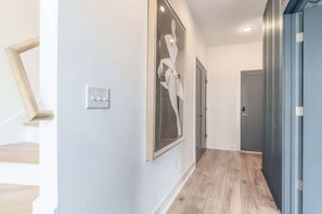 A hallway with a wooden staircase on the left, a framed artwork on the wall, and a door at the end.