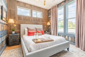 A modern bedroom with a large bed, bedside tables, a dresser, and a view of the outdoors.