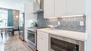 A modern kitchen with stainless steel appliances, white cabinetry, and a patterned backsplash.