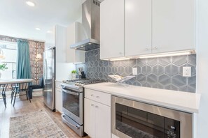 A modern kitchen with stainless steel appliances, white cabinetry, and a patterned backsplash.