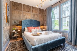 A modern bedroom with a large bed, wooden panel walls, and a view of the outside.
