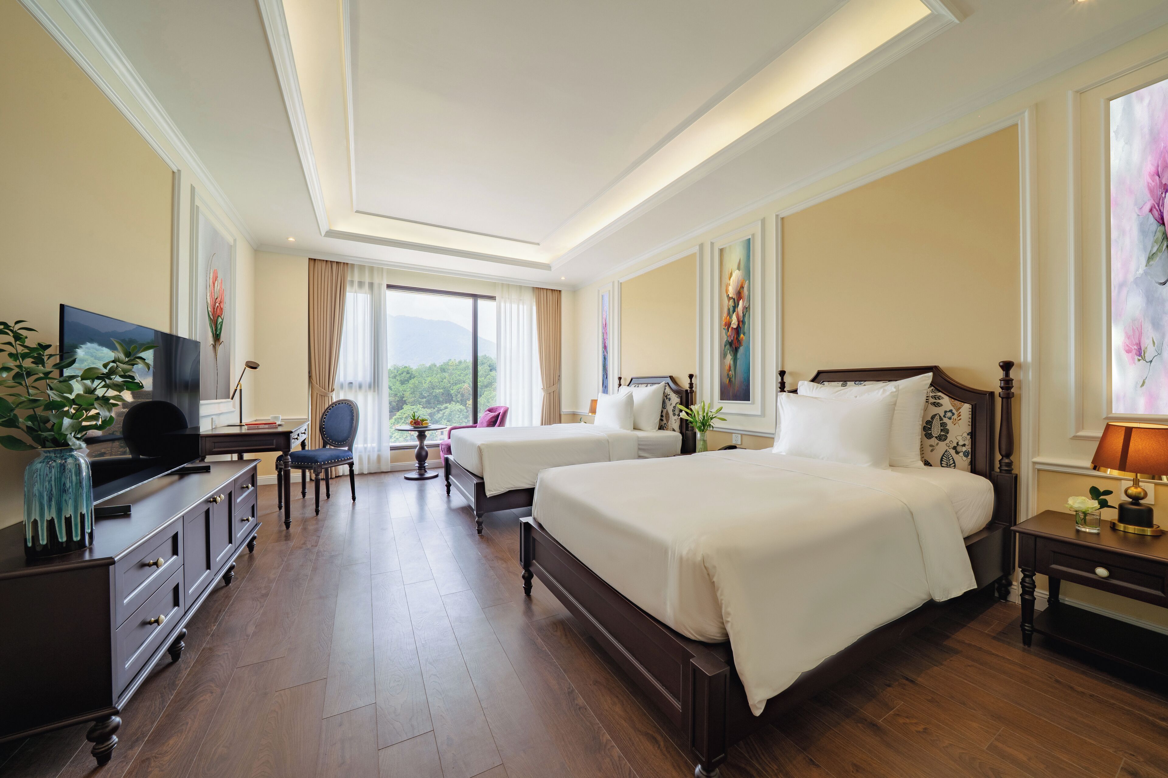 A hotel room with two beds, a desk, a chair, a TV, and a large window with a view.