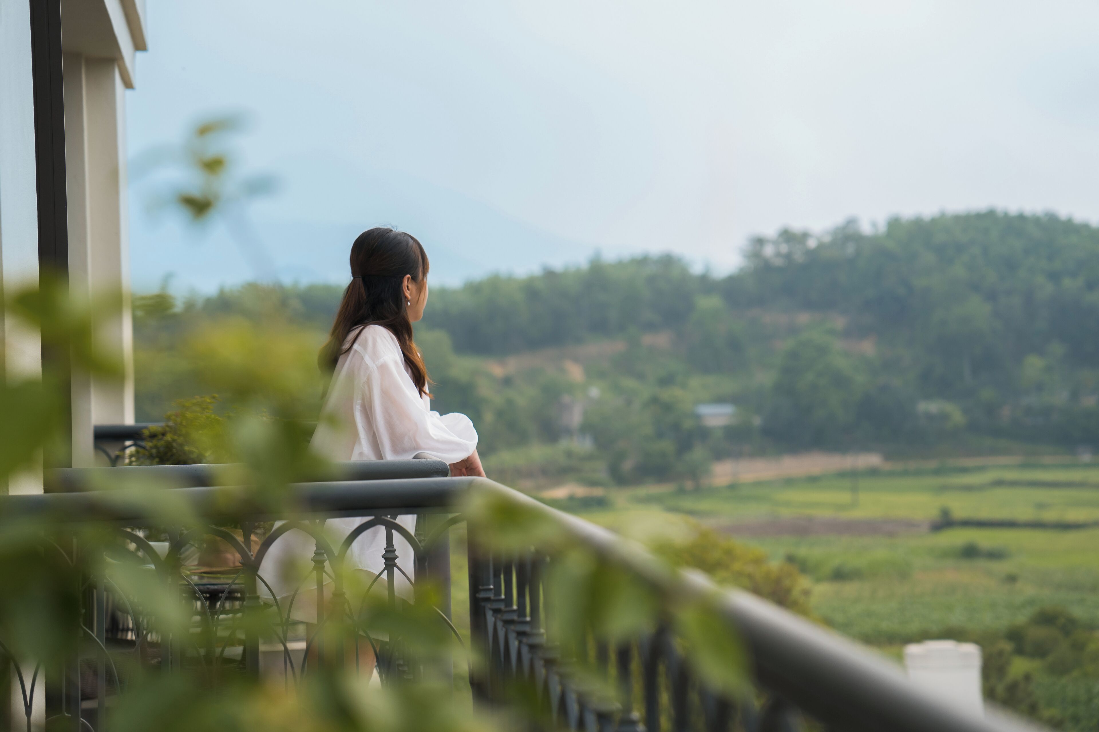 A person sitting on a balcony overlooking a green landscape.