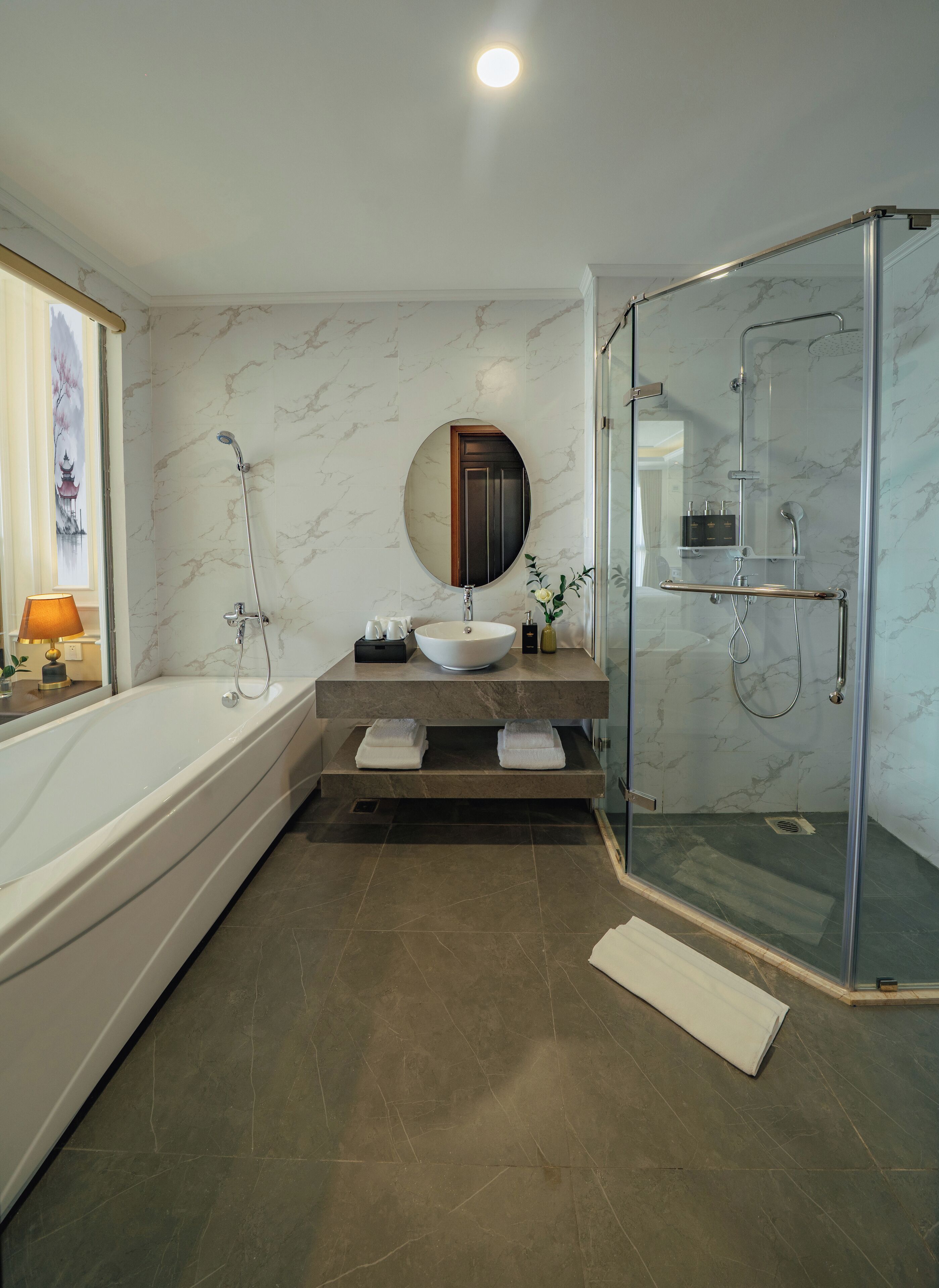 Un baño moderno con bañera, espejo redondo, ducha con mampara de vidrio y paredes con diseño de mármol.