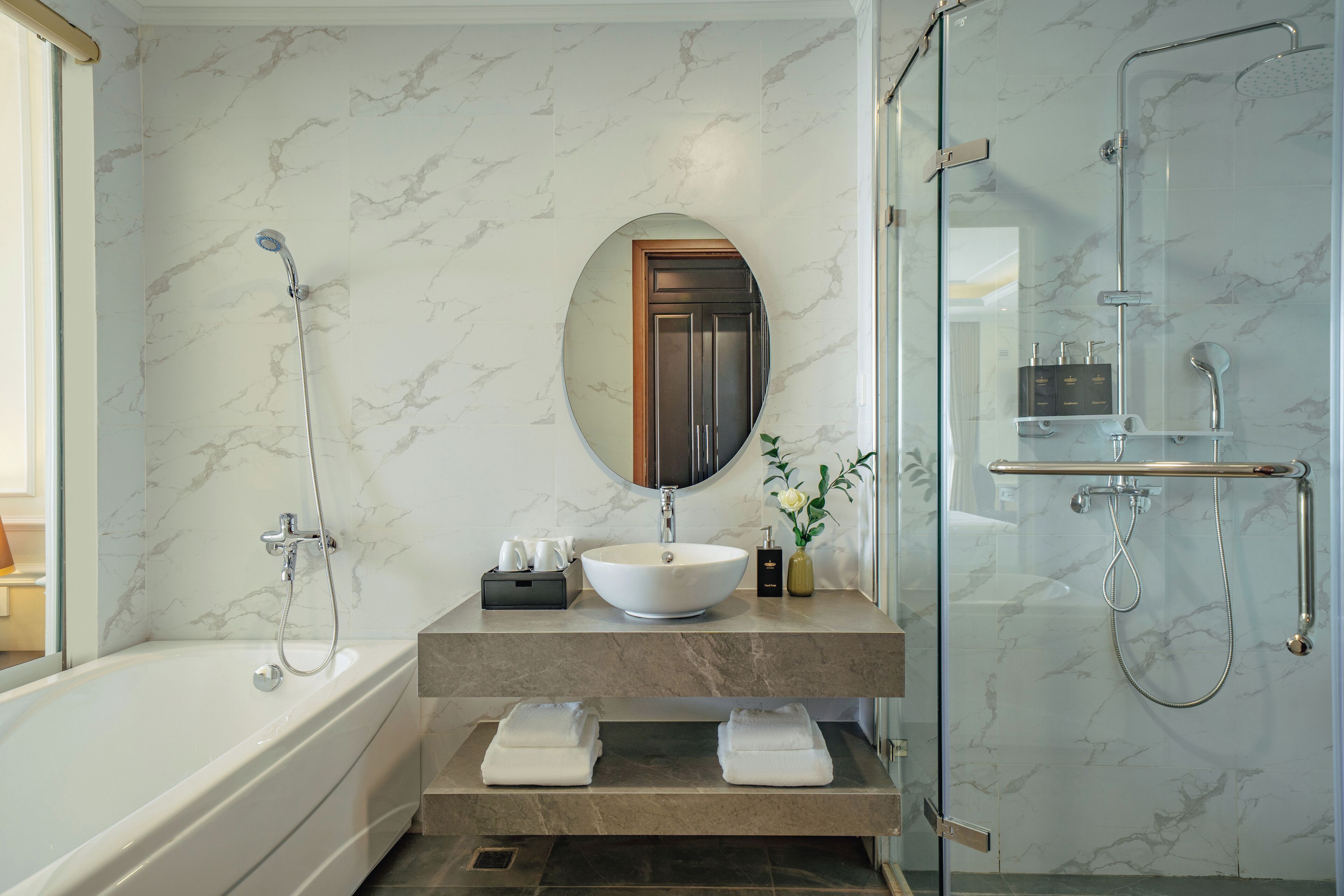 Une salle de bain moderne avec une baignoire, un miroir rond, un lavabo et une douche à parois de verre.
