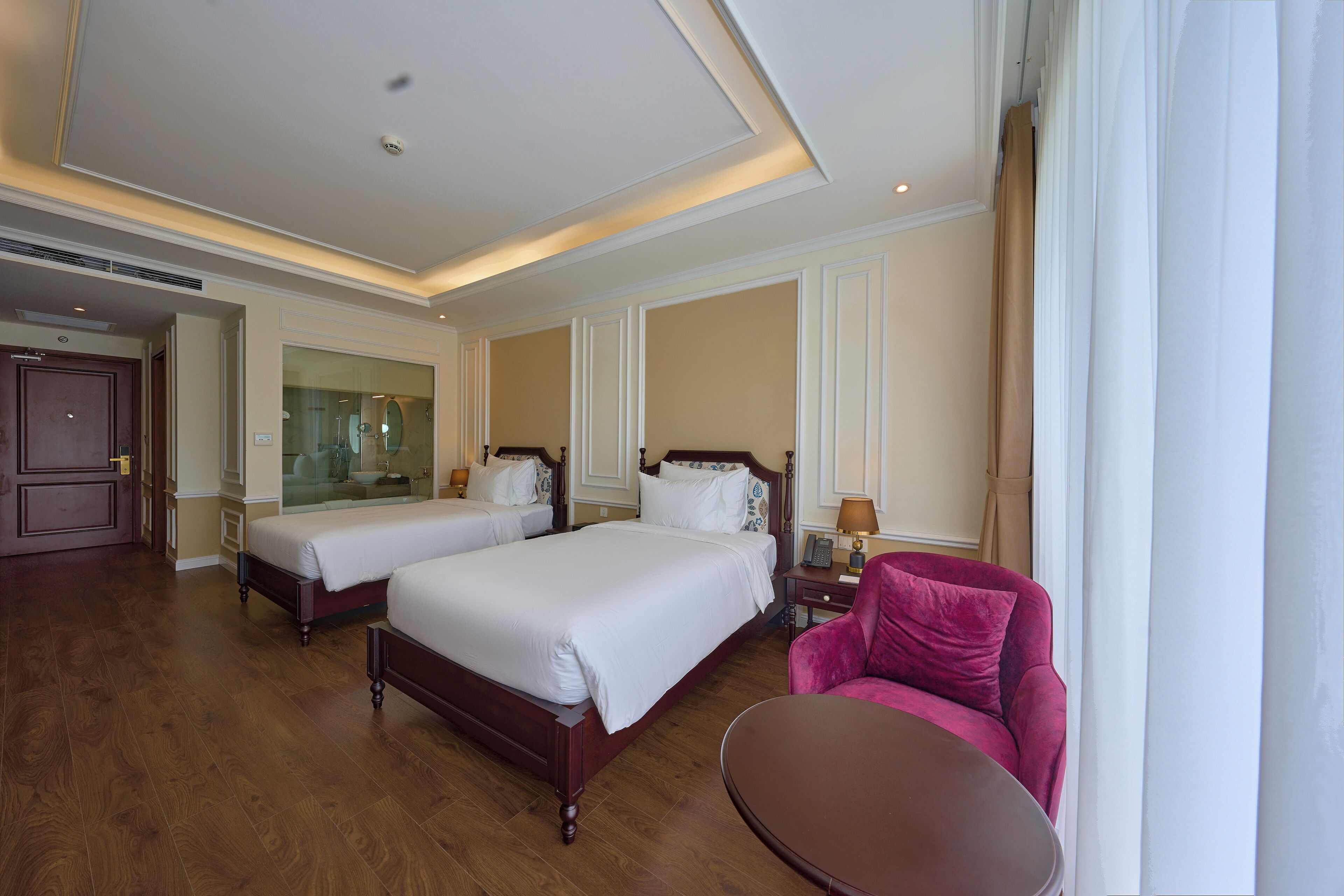 A hotel room with two beds, a sitting area with a chair and table, and a large mirror.