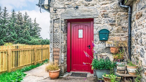 Un edificio de piedra con una puerta roja, una cerca de madera y varias plantas en macetas.