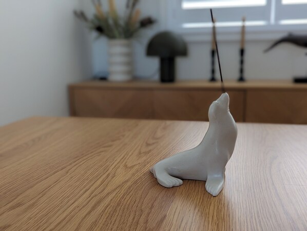 Une sculpture de loup en céramique est posée sur une table en bois dans une pièce dotée d’une fenêtre, et un vase rempli de fleurs se trouve à l’arrière-plan.