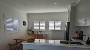 A modern kitchen with a central island, two bar stools, and a dining table. - Stylish Seaside Retreat with Spa (Narooma)