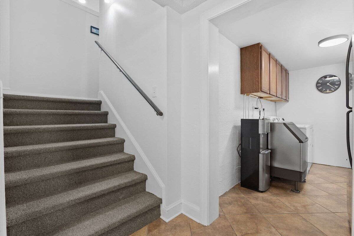 Eine Treppe führt zu einem Küchenbereich mit einem Kühlschrank und einer Uhr an der Wand.