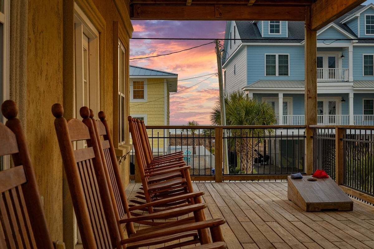 A wooden deck with chairs, a small table, and a view of neighboring houses.