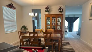 A dining area with a pool table, chairs, and a cabinet with glass doors.