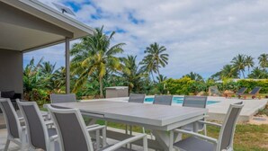 A covered outdoor dining area with a table and chairs, a pool, and palm trees in the background. - Enua Tipani Pool Villa
• Quiet • Convenient location• Modern Finishes • Sleeps 8 (Rarotonga)