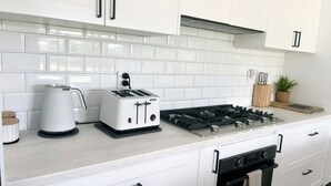 A modern kitchen with white cabinets, a gas stove, a toaster, and a kettle. - Enua Tipani Pool Villa
• Quiet • Convenient location• Modern Finishes • Sleeps 8 (Rarotonga)