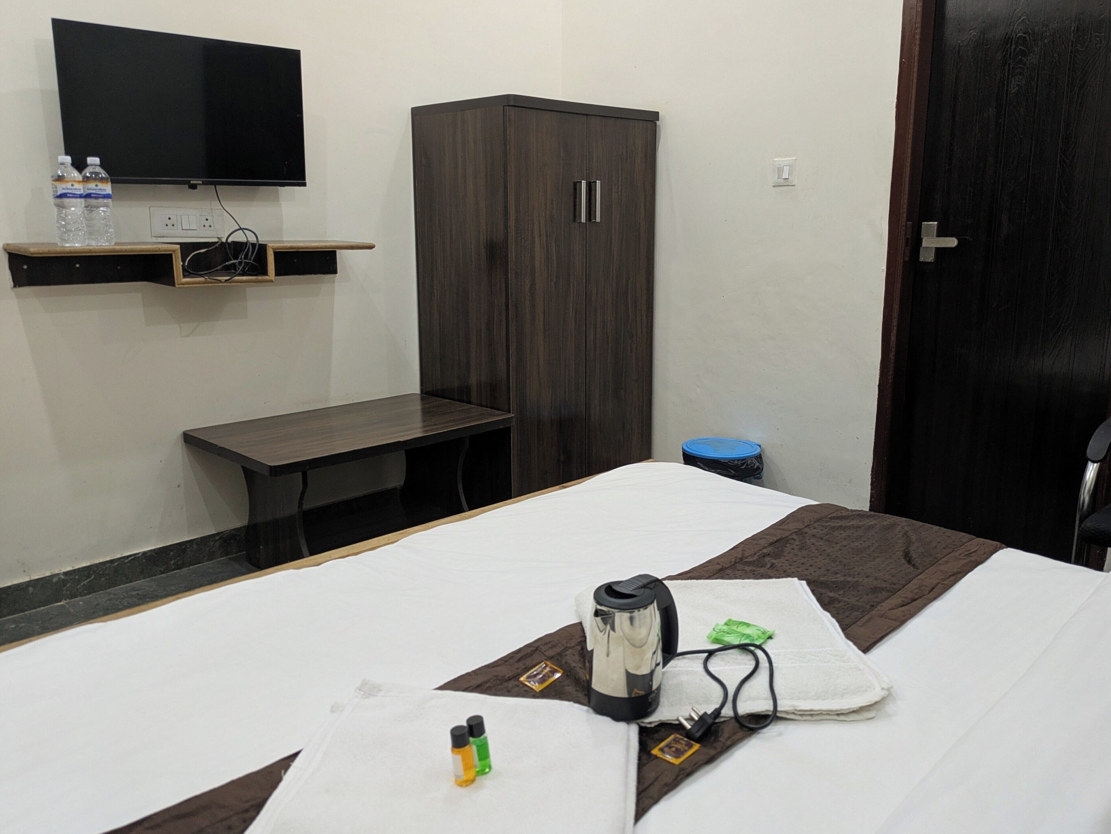 A hotel room with a bed, a desk, a wardrobe, a television, and a water dispenser.