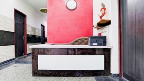 Un mostrador de recepción con un reloj, una estatua y un altavoz negro sobre un suelo de mármol.