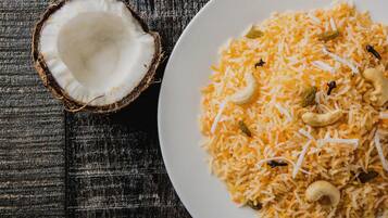 Un plato de arroz amarillo con anacardos y pasas, y medio coco sobre una superficie de madera.