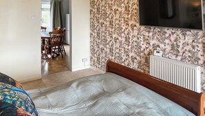 A bedroom with a bed, a TV mounted on the wall, a radiator, and a dining area in the background. - 1 bedroom accommodation in St Athan , near Cardiff (St Athan , near Cardiff)
