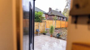 A patio area with a wooden fence, potted plants, and a brick wall in the background. - 3bedroom-sleeps5-wifi-singlecarparking (Manchester)