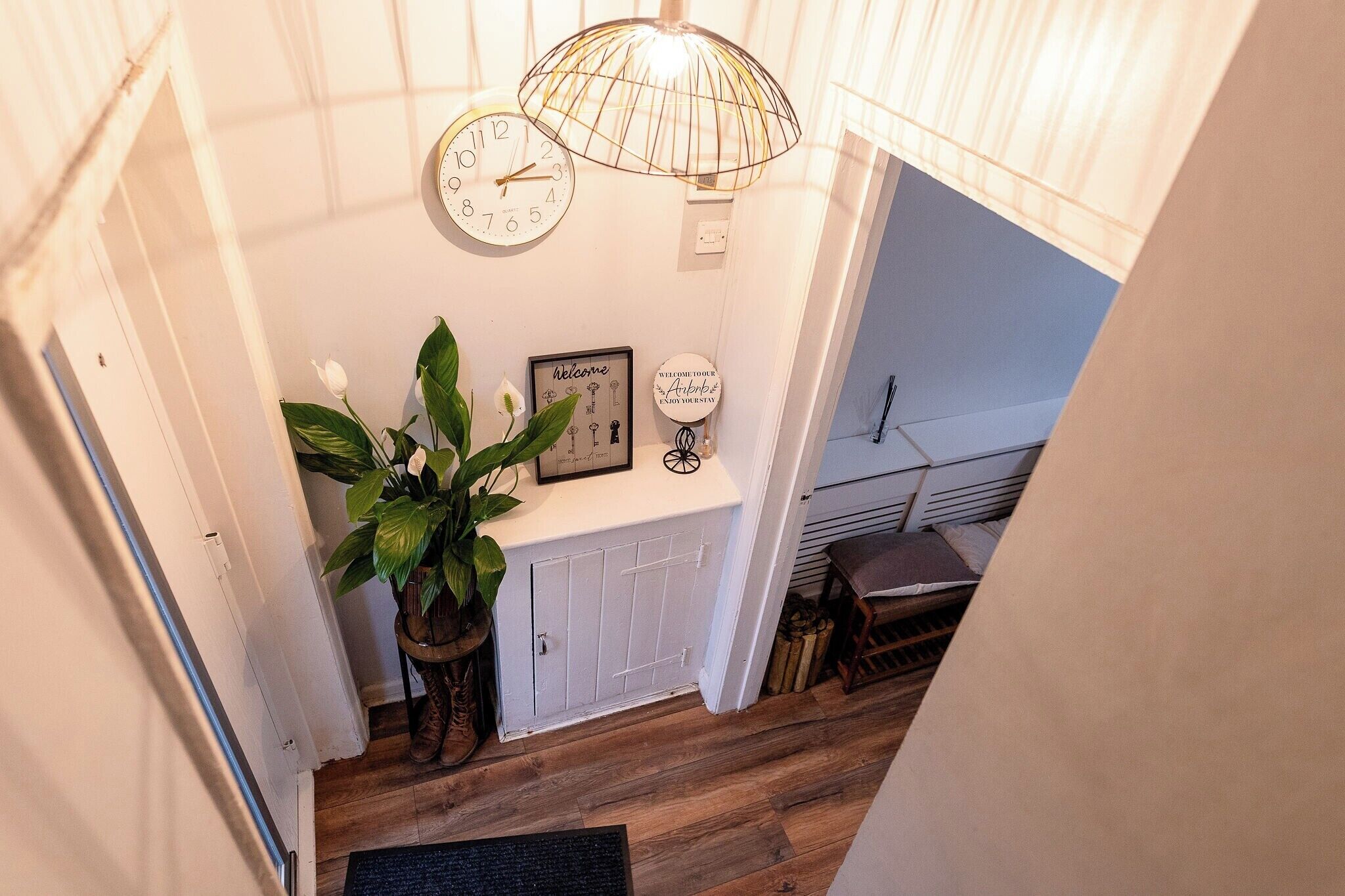 A staircase with a wooden floor, a white door, a potted plant, a clock, and a welcome sign.