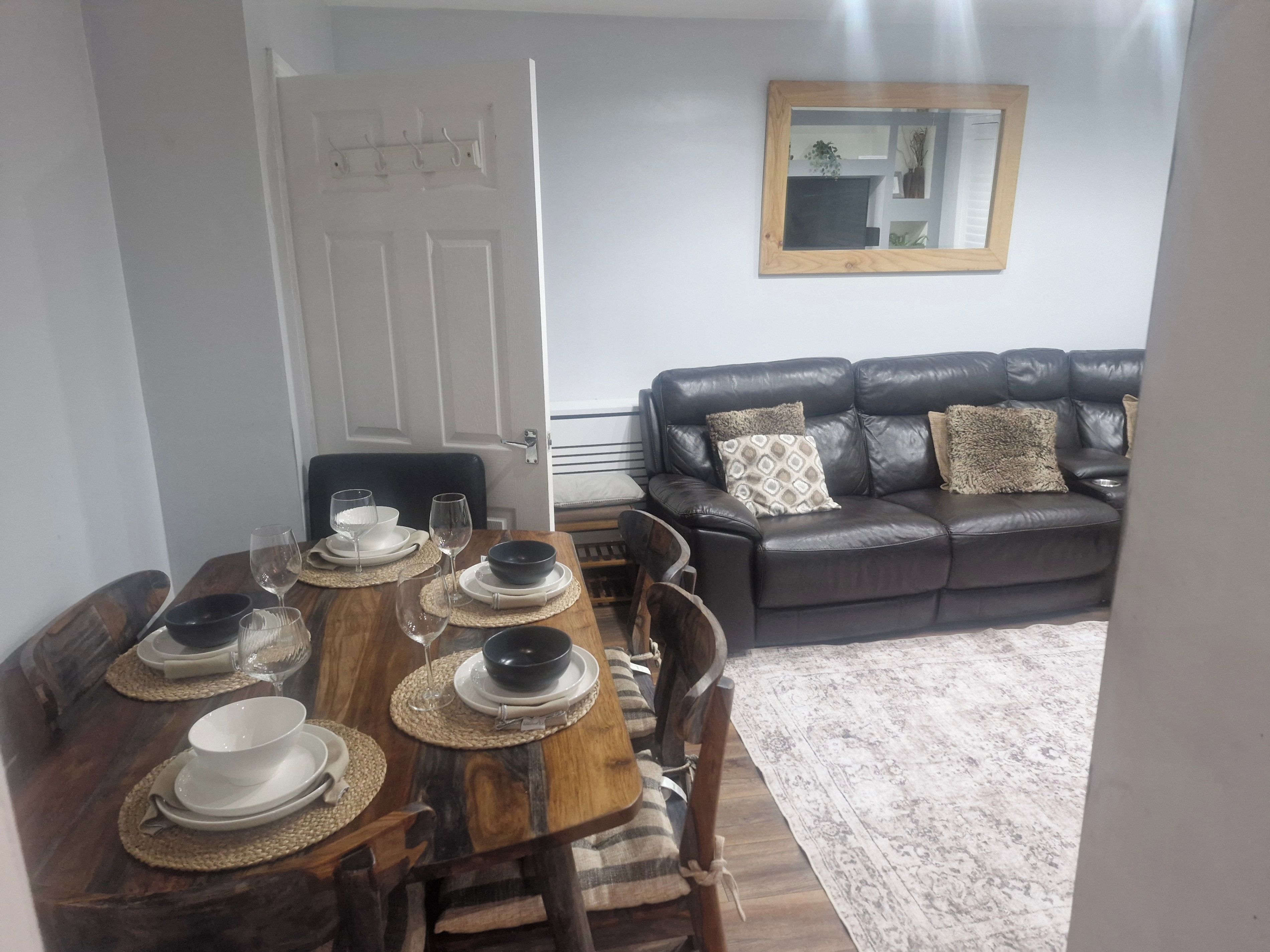A dining area with a wooden table set for four, a black leather sofa, and a mirror on the wall.