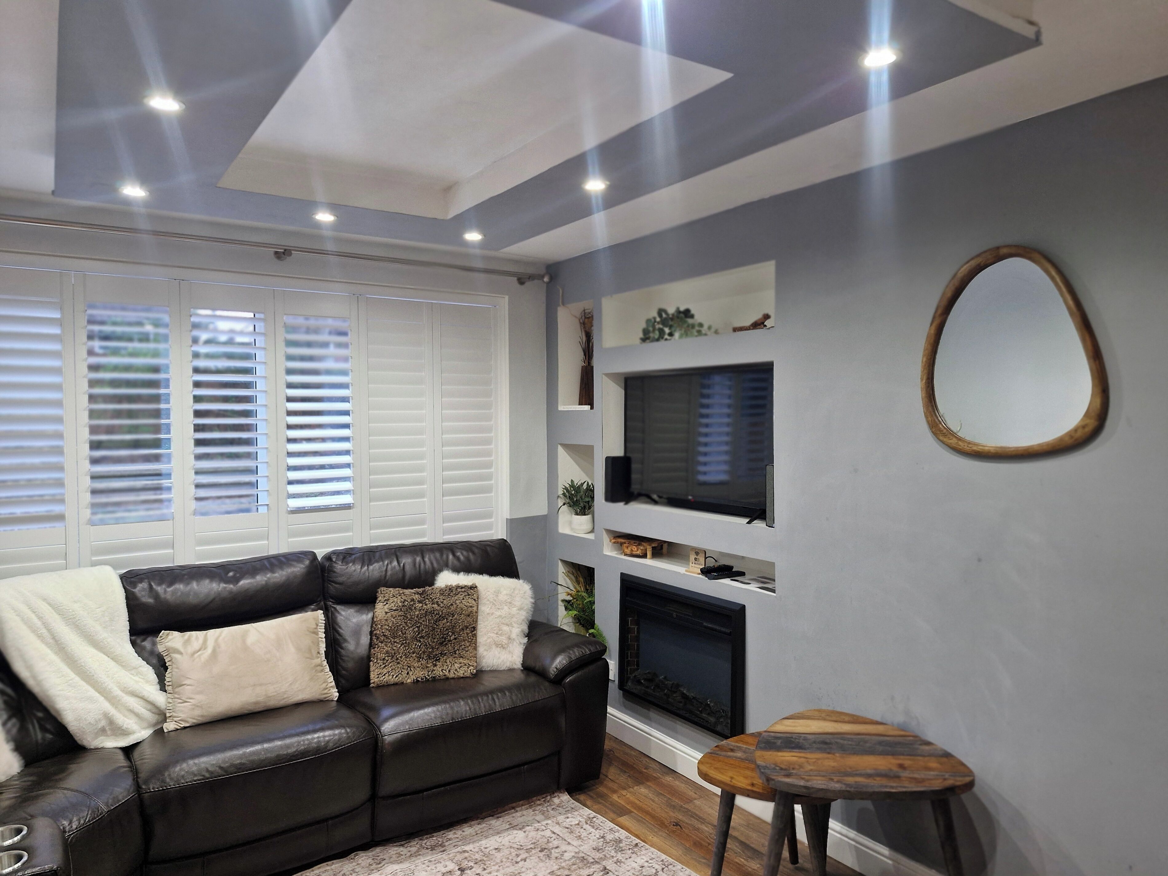 A living room with a black leather sofa, a small wooden stool, a fireplace, and a mounted television.