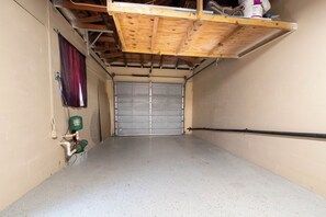 Garagem com porta fechada, piso de concreto e estrutura de teto em madeira.