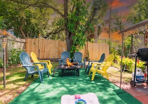 An outdoor patio with a fire pit, green artificial turf, and colorful Adirondack chairs.
