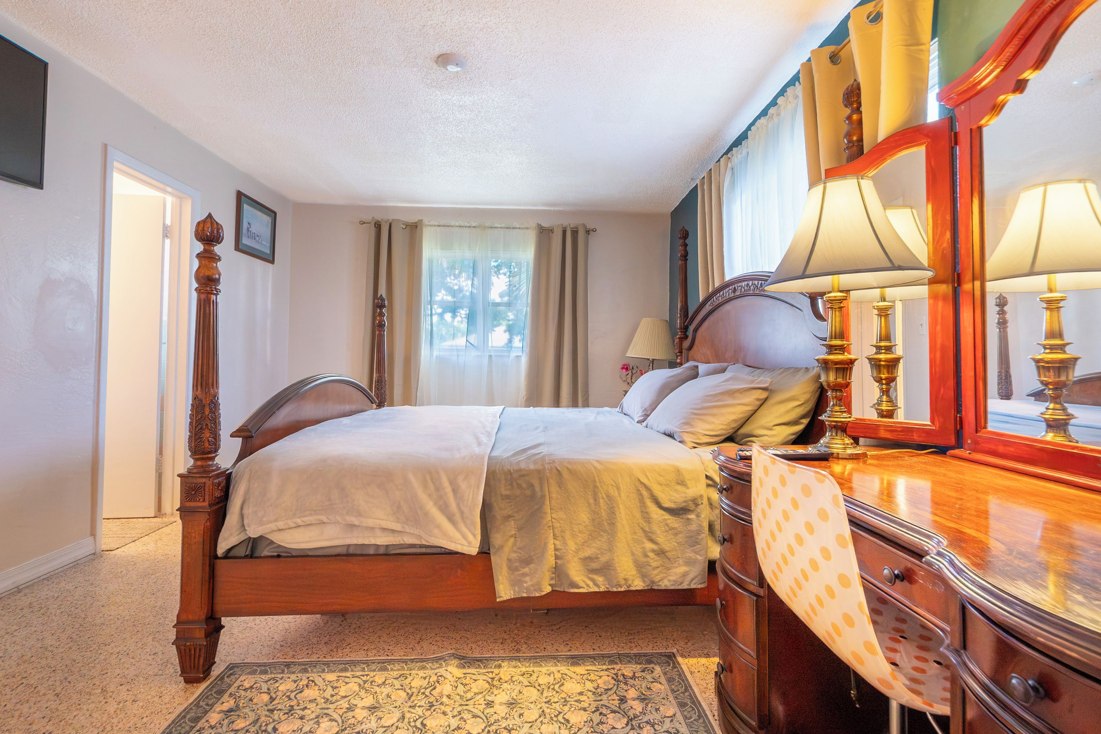 A bedroom with a bed, a dresser, a mirror, and a window with curtains.