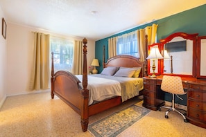 A bedroom with a four-poster bed, a desk with a chair, and a large mirror.