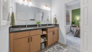 Een moderne badkamer met een dubbele wastafel, houten kastjes, een grote spiegel en een groene accentmuur.