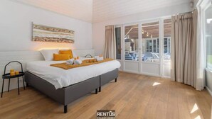 Ein modernes Schlafzimmer mit einem großen Bett, einem Nachttisch mit Kerzen und Blick ins Freie durch eine Schiebetür.