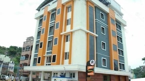A multi-story hotel with a modern architectural design, featuring a prominent orange and grey color scheme. - SSR HOTEL (Srikalahasti)