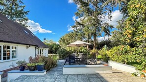 A patio area with a table and chairs, surrounded by potted plants and a white wall. - 4 bedroom accommodation in Welshpool (Welshpool)