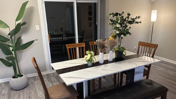 Een eetgedeelte met een marmeren tafel, houten stoelen, een bank en potplanten.
