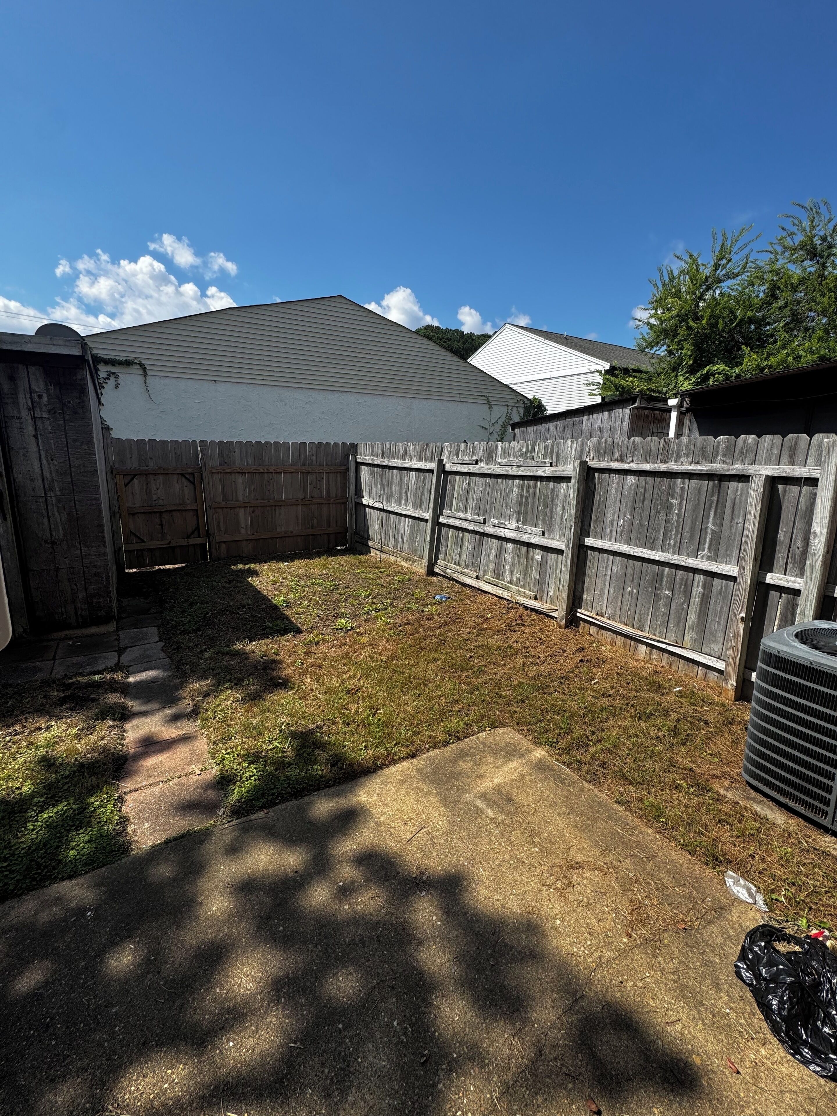 A backyard with a wooden fence, a concrete patio, and a white building in the background.