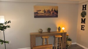 Een knus vertrek met een houten bureau, twee krukken, een potplant en een wandeling schilderij.
