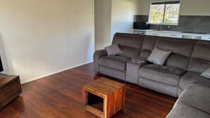 Un salon avec un canapé gris, une table basse en bois et, au fond, un coin cuisine.