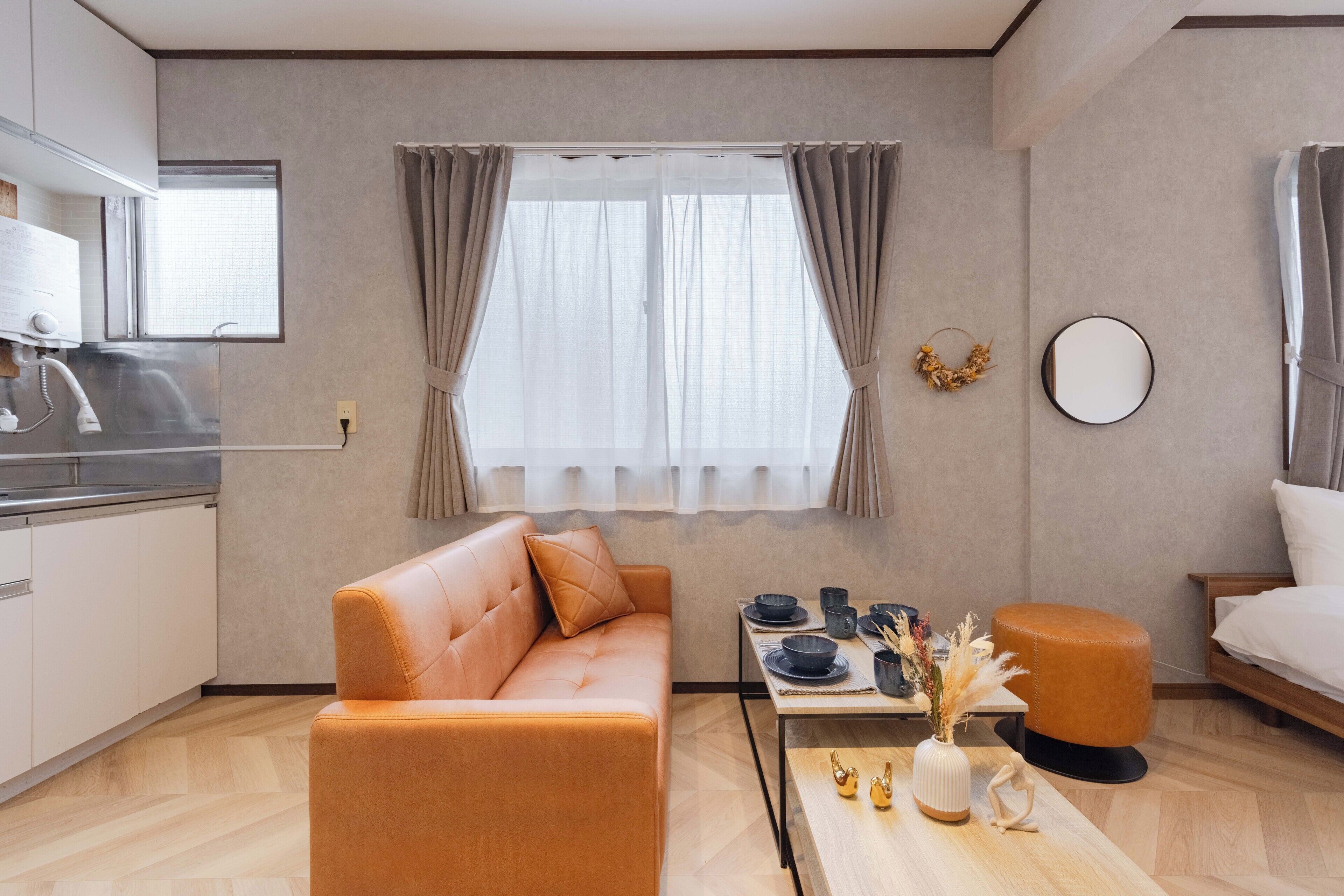 Un salon moderne comprenant un canapé, une table à manger avec des chaises, une petite table ronde agrémentée d’objets décoratifs, un miroir rond et une fenêtre avec des rideaux.