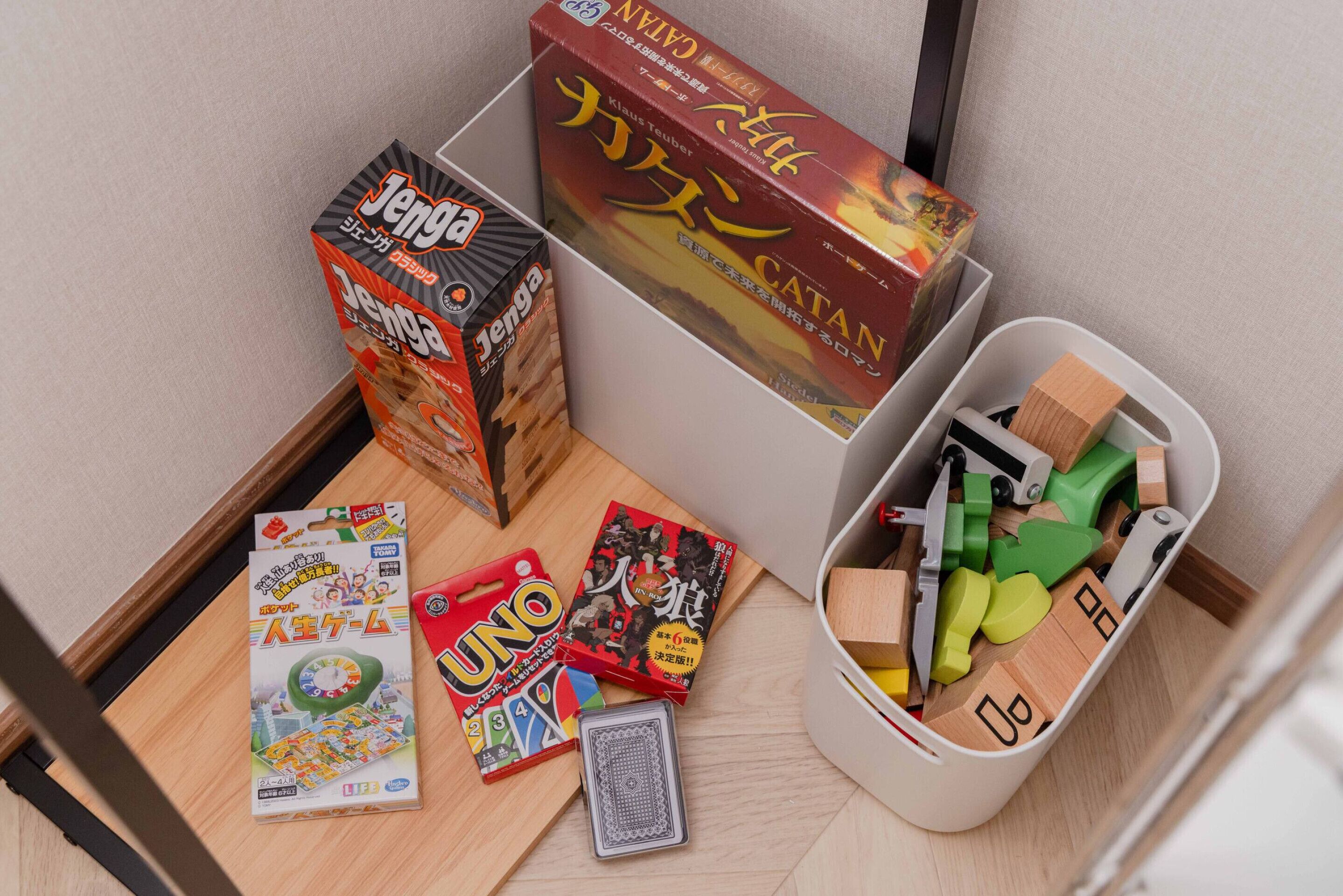 A tabletop with various board games, including Jenga, Catan, and UNO, along with a box of Mahjong tiles.