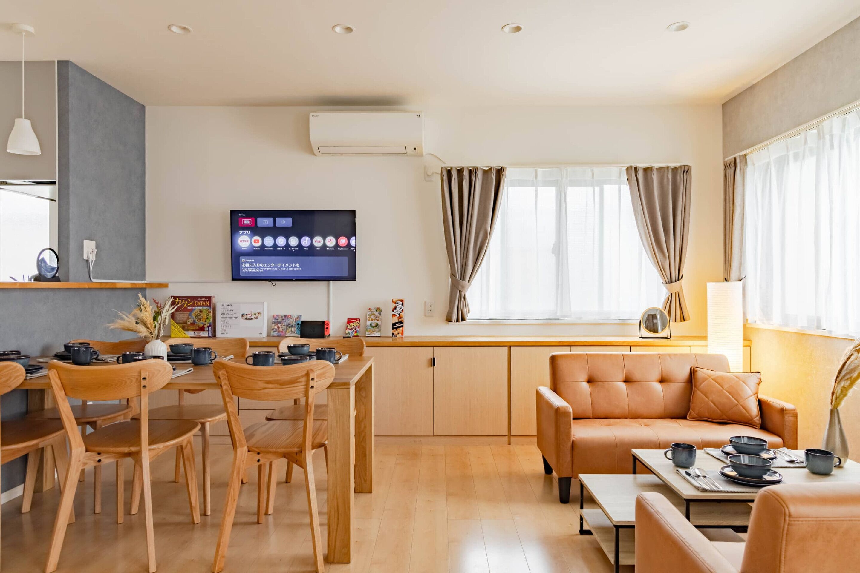 A modern living room with a sofa, dining table, chairs, a flat-screen TV, and a window with curtains.