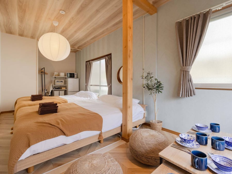 A bedroom with a wooden bed, a bedside table with blue and white dishes, a hanging light fixture, and a window with curtains.
