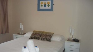 A neatly made bed with towels, a framed picture of flowers, and bedside lamps. - Sails Resort on Golden Beach Unit 03 (Golden Beach)