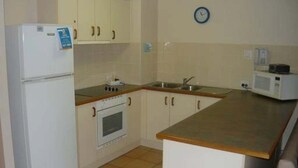 A compact kitchen with white cabinets, a built-in oven, a microwave, and a sink. - Sails Resort on Golden Beach Unit 03 (Golden Beach)