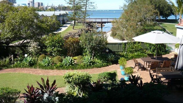 A garden with a view of the sea, a wooden deck, and outdoor seating. - Sails Resort on Golden Beach Unit 03 (Golden Beach)
