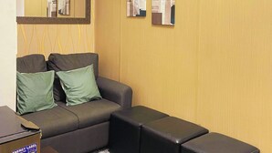 A room with a sofa, two pillows, a small table, and a mirror on the wall. - Charm's City Escape at Grace Residences (Taguig)