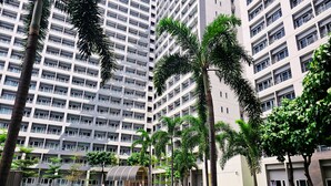 A modern apartment building with a swimming pool, palm trees, and a covered outdoor area. - Charm's City Escape at Grace Residences (Taguig)