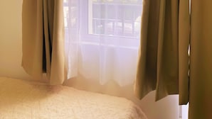 A bedroom with a bed, beige curtains, and a window with a view of buildings. - Charm's City Escape at Grace Residences (Taguig)
