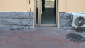 A building entrance with a glass door, a plaque on the wall, and an air conditioning unit outside.